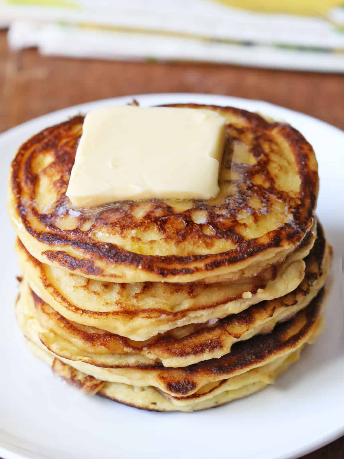 Keto ricotta pancakes are stacked on a white plate and topped with butter.