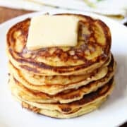 Keto ricotta pancakes are stacked on a white plate and topped with butter.