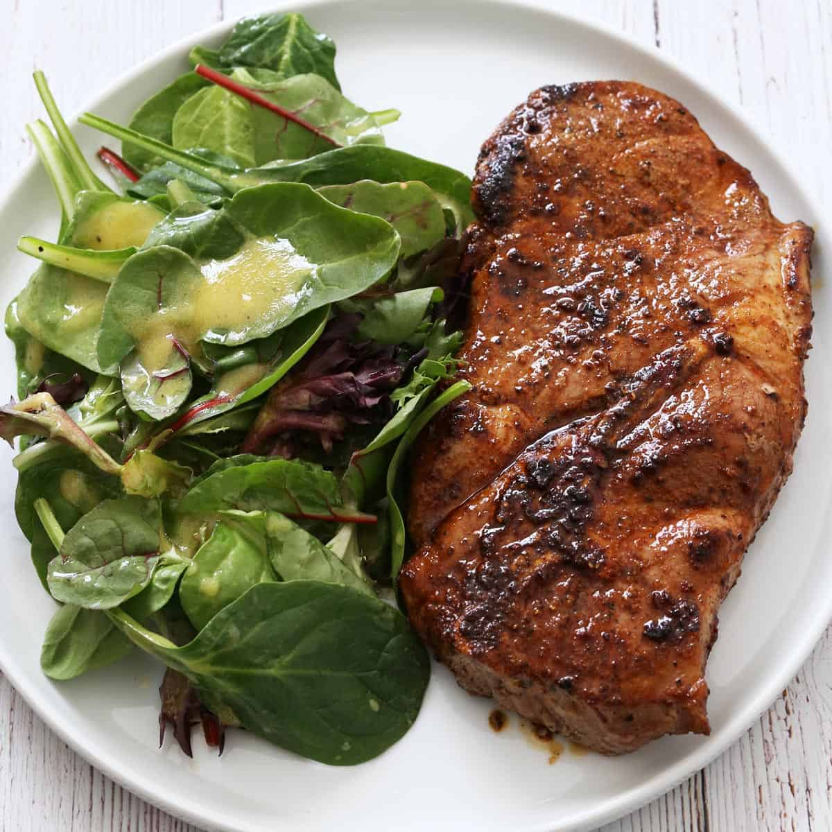 A pork steak is served on a white plate with a salad.