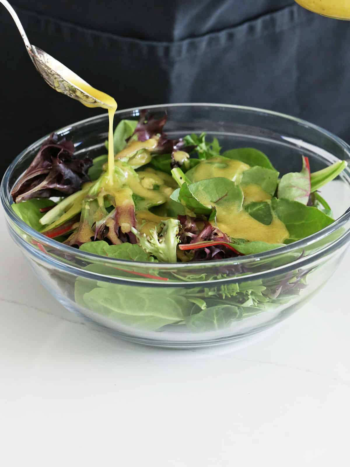 Pouring the dressing on mixed salad greens in a bowl.