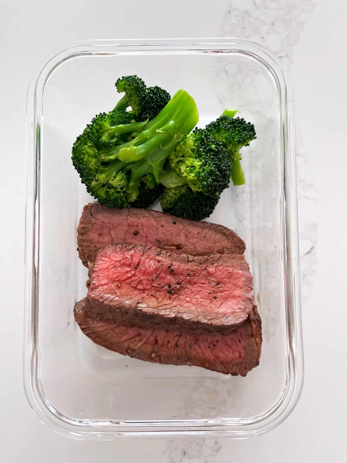 Leftover sirloin steak with broccoli in a glass container.