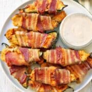 Stuffed jalapenos are served on a plate with a dip.