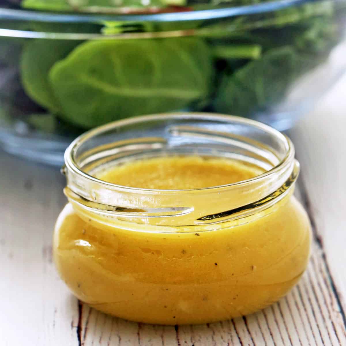 Vinaigrette is served in a jar next to a bowl with mixed salad greens.