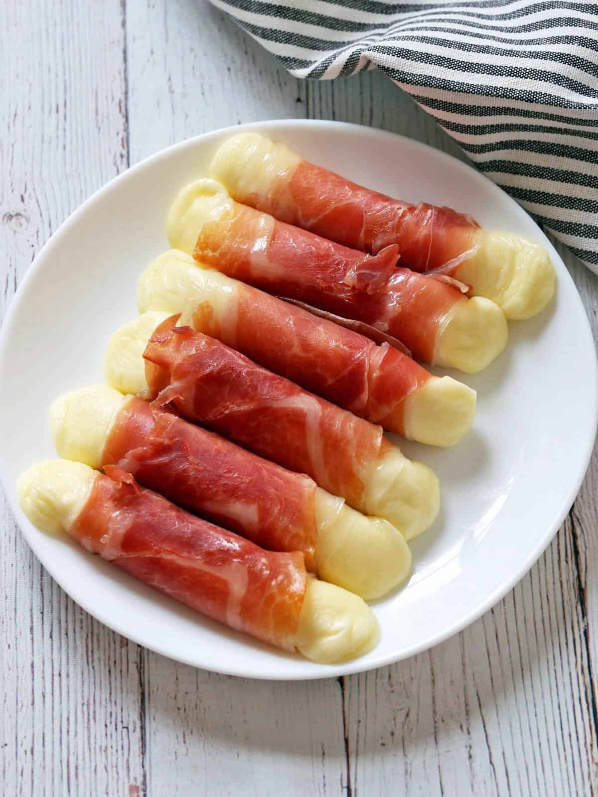 Prosciutto wrapped mozzarella is served on a white plate.