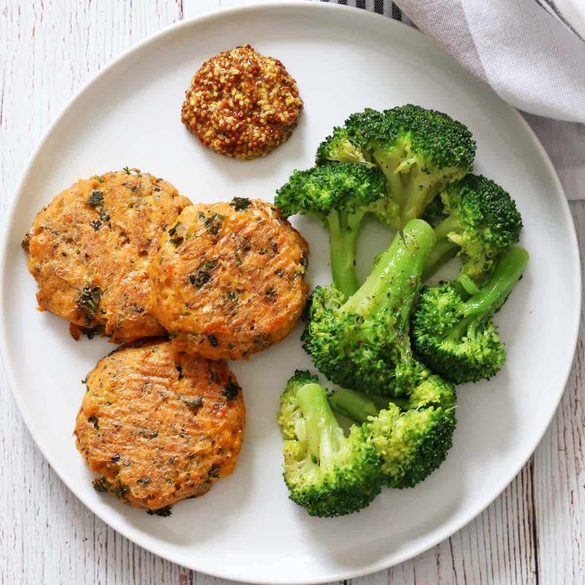 Salmon cakes are served with mustard and broccoli.