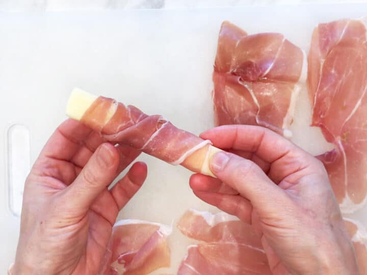 Wrapping a mozzarella stick with a slice of prosciutto.