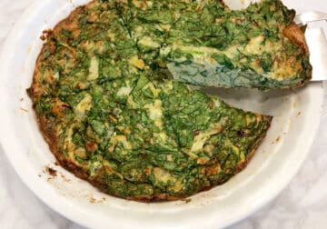 Lifting a slice of spinach frittata from the pan.