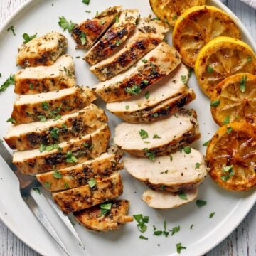 Greek chicken is served with lemon slices.
