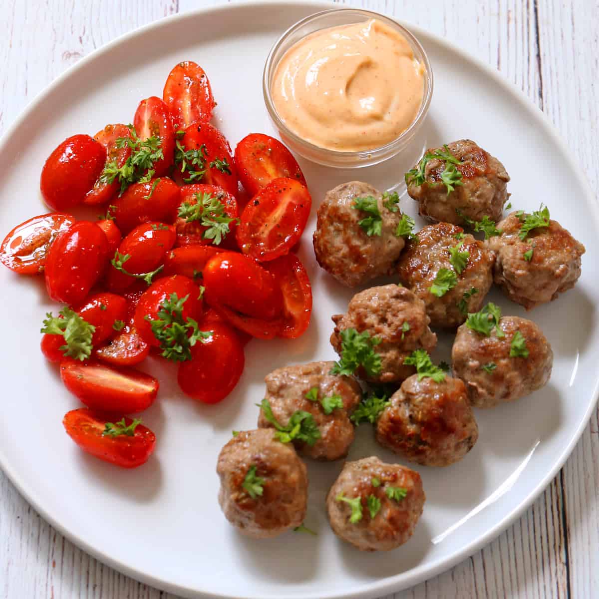 Lamb meatballs are served with tomato salad and sriracha mayo.