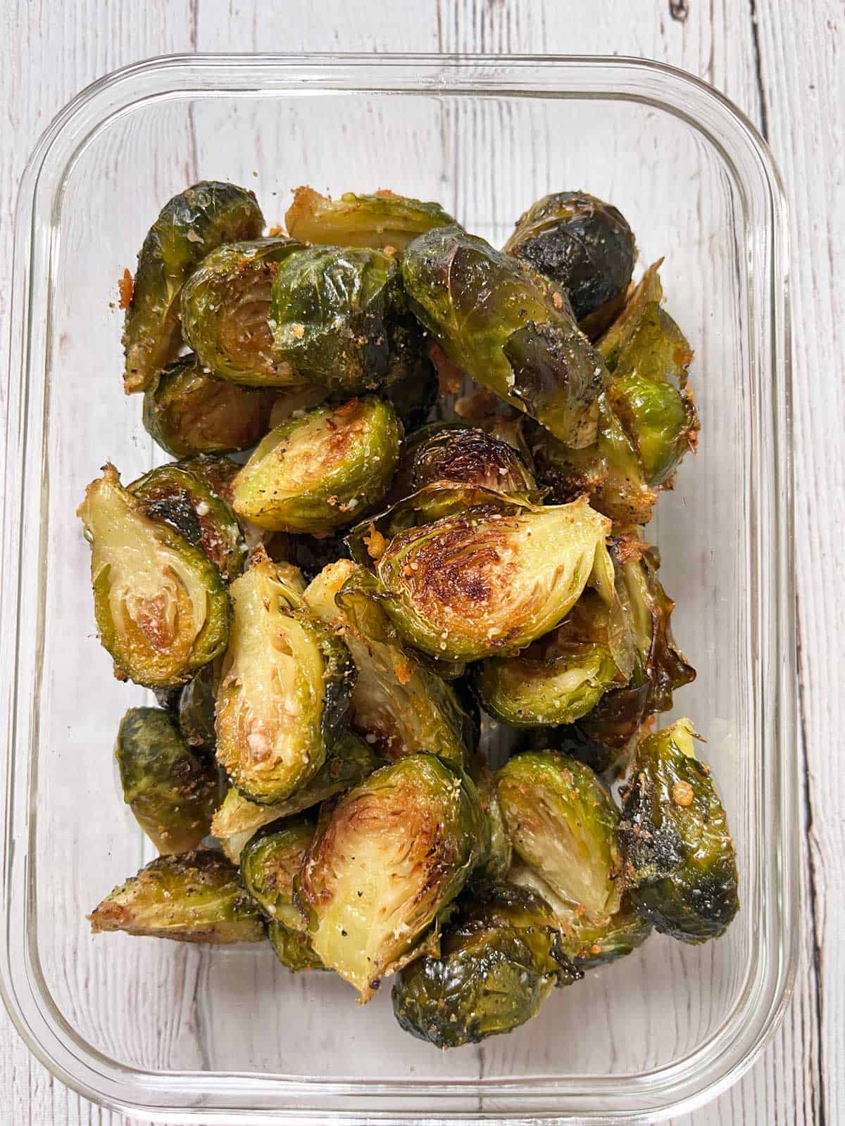 Roasted Brussels sprouts with parmesan are stored in a glass storage container.