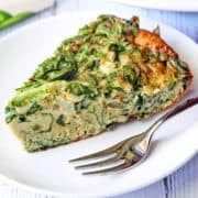 A slice of spinach frittata is served on a white plate with a fork.