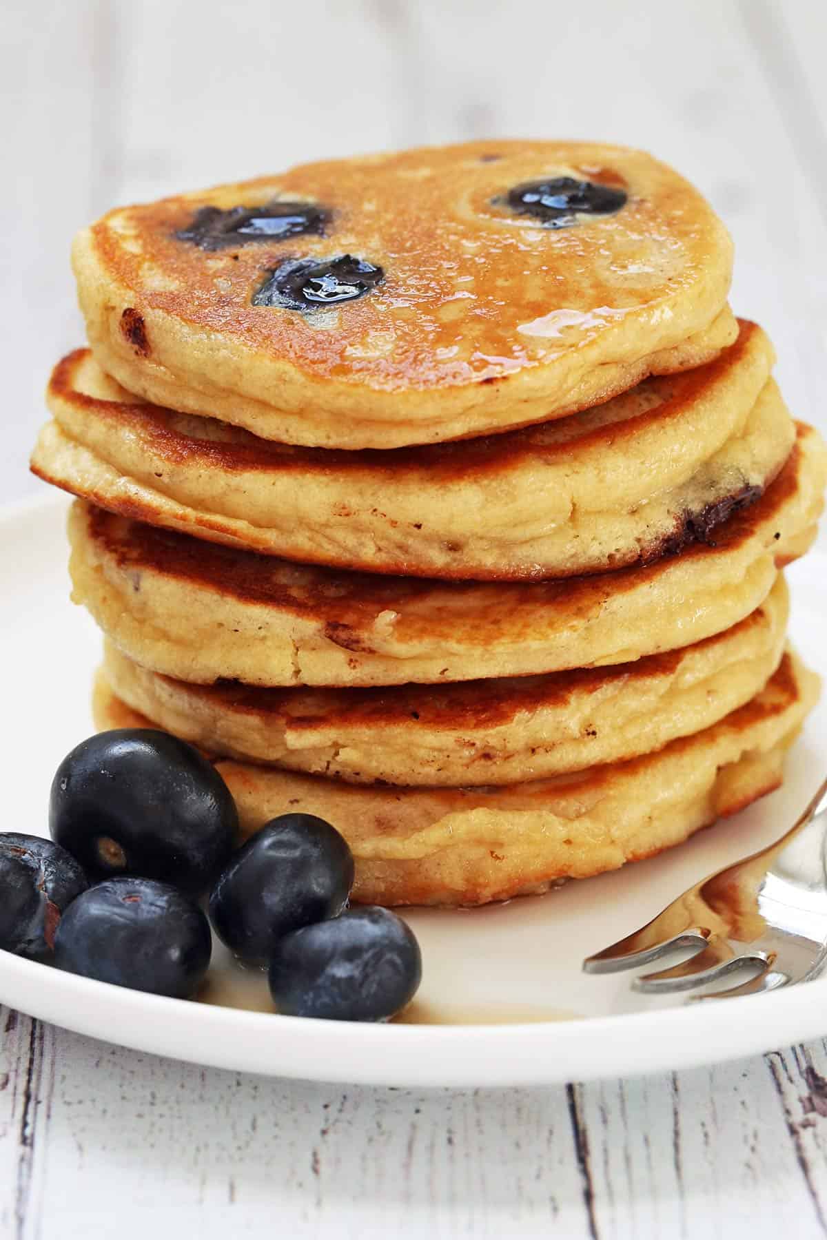 Almond flour pancakes are stacked on a plate and served with fresh blueberries.