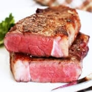 A reverse-seared steak was cut in two and is served on a white plate with a serving fork.