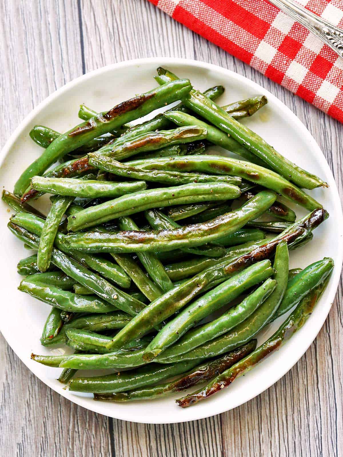 Roasted green beans are served on a white plate with a red napkin.