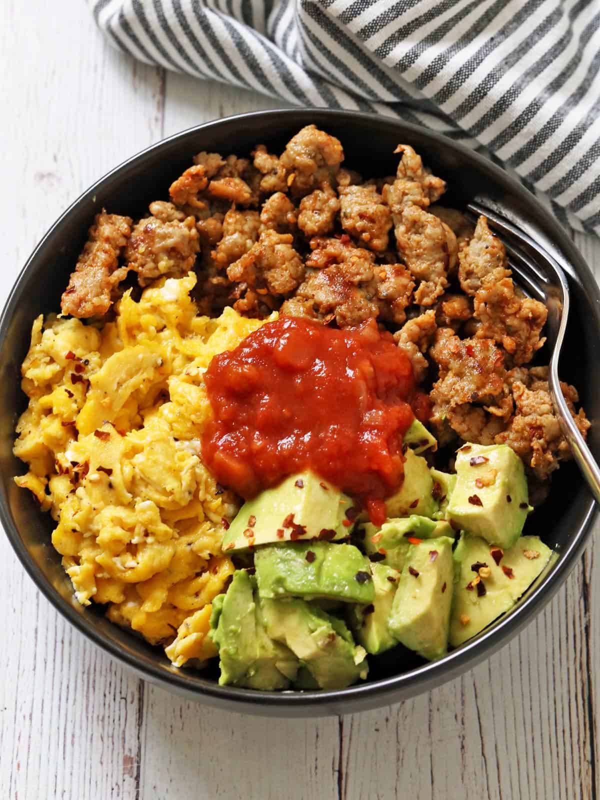 A breakfast bowl with sausage, eggs, and avocado is topped with salsa.
