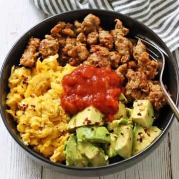 A breakfast bowl with sausage, eggs, and avocado is topped with salsa.