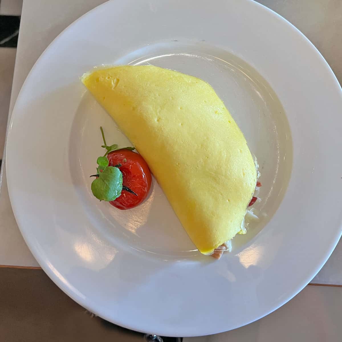A perfectly cooked French omelette is served on a plate with a tomato.