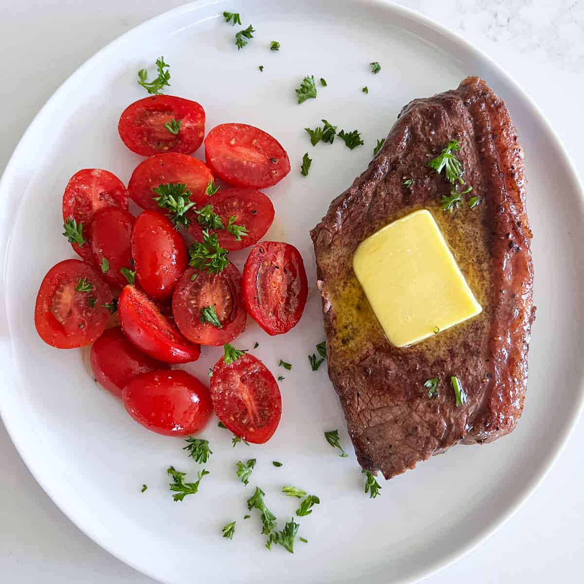 Picanha steak is topped with butter and served with tomato salad.