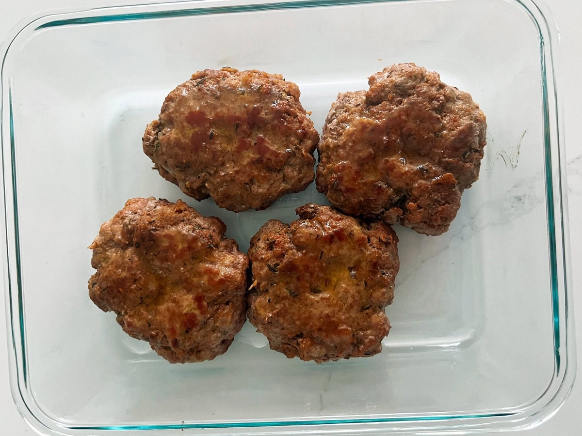 Leftover pork burgers in a glass food storage container.