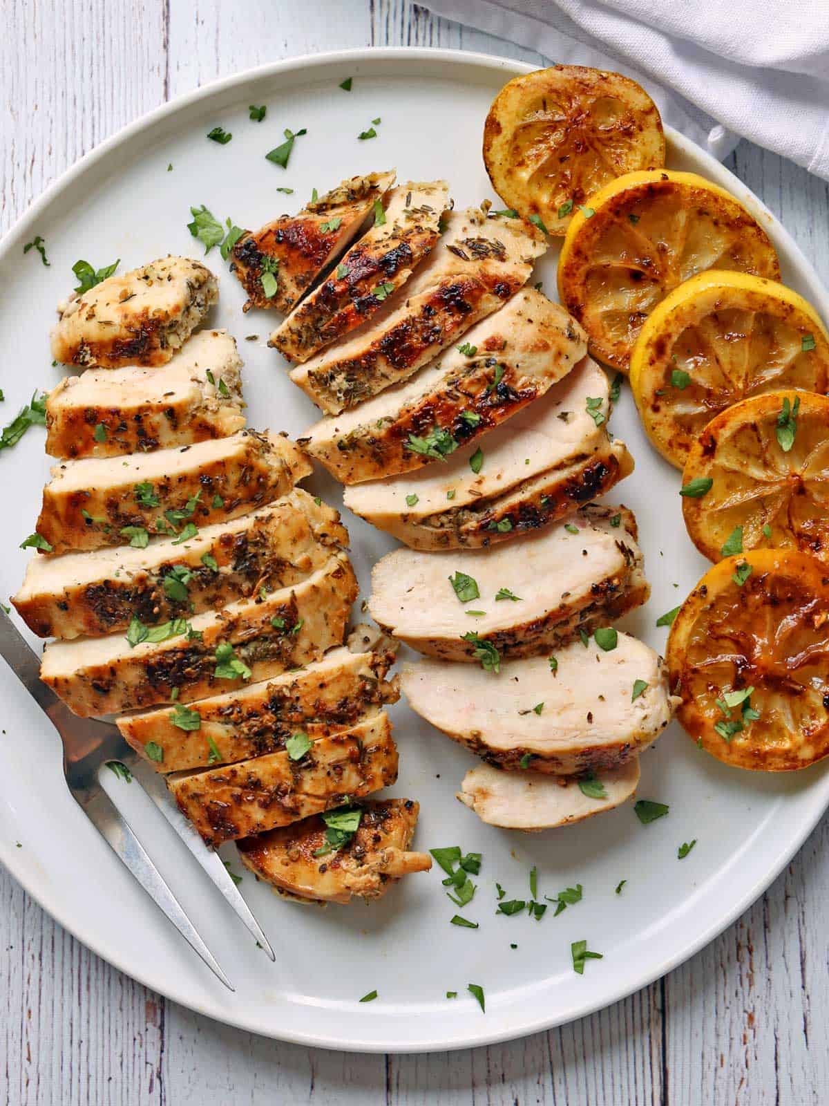 Sliced Greek chicken is served with lemon slices.