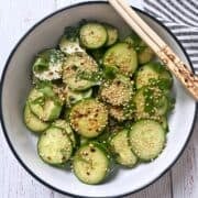 Asian cucumber salad is served in a white bowl with chopsticks.