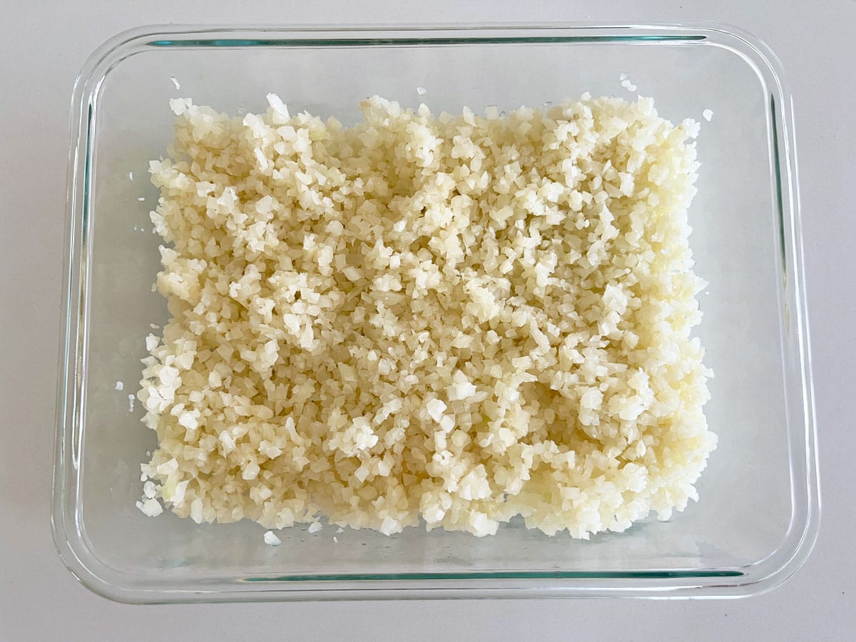 Cauliflower rice leftovers are kept in a glass food storage container.