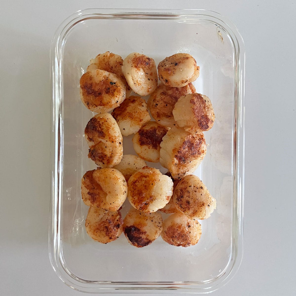 Leftover grilled scallops are stored in a glass food storage container.