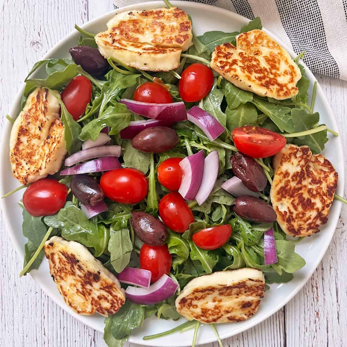 An arugula salad is topped with slices of pan-fried halloumi cheese.