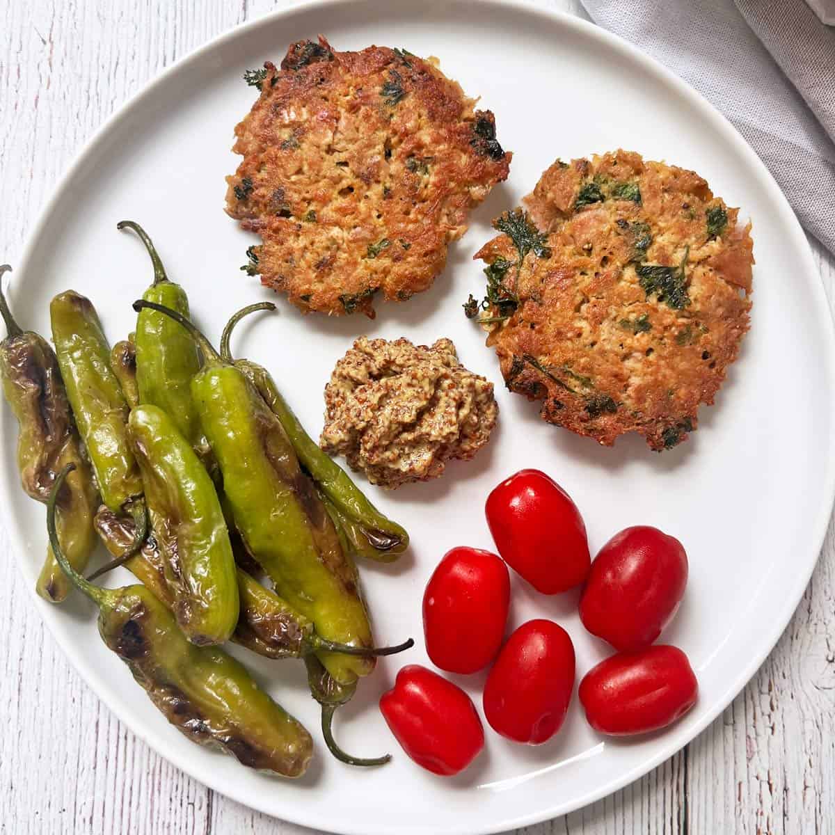 Leftover tuna patties are served with shishito peppers, tomatoes, and grainy mustard.