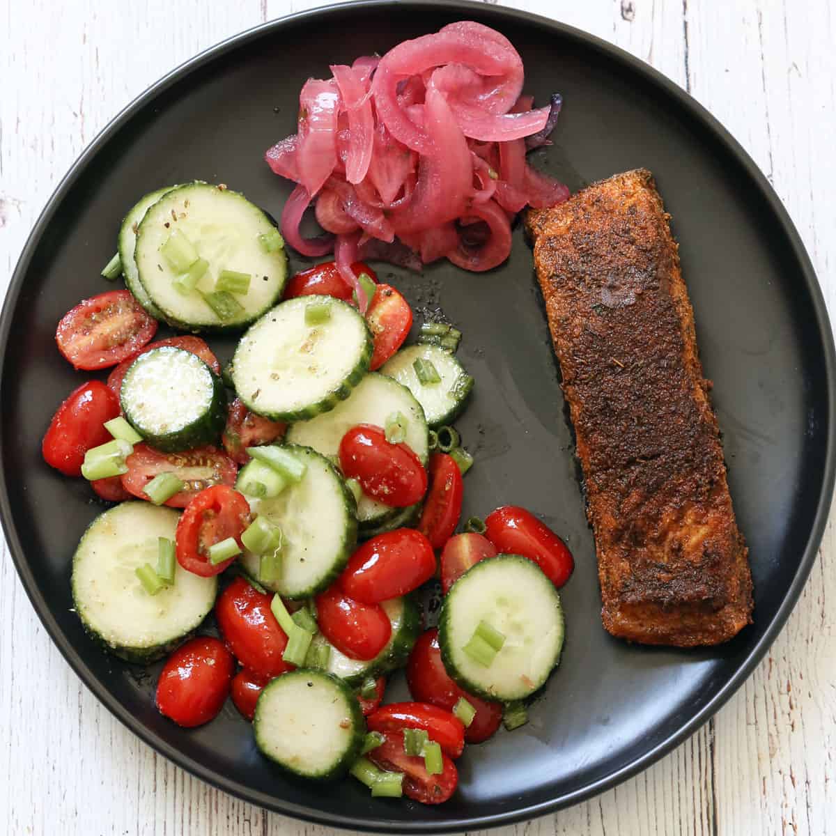 Blackened salmon is served with cucumber tomato salad and pickled red onions.