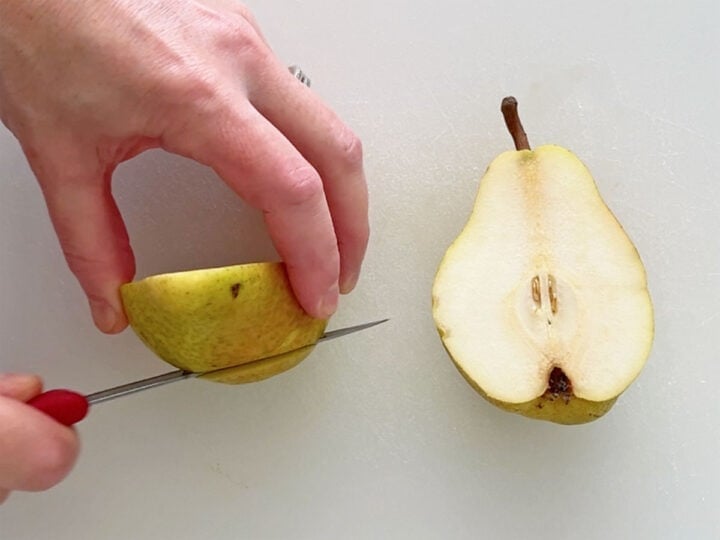 Shaving a thin slice off the peel side of each pear half.
