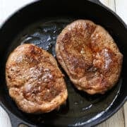 Two lamb steaks in a cast-iron skillet.