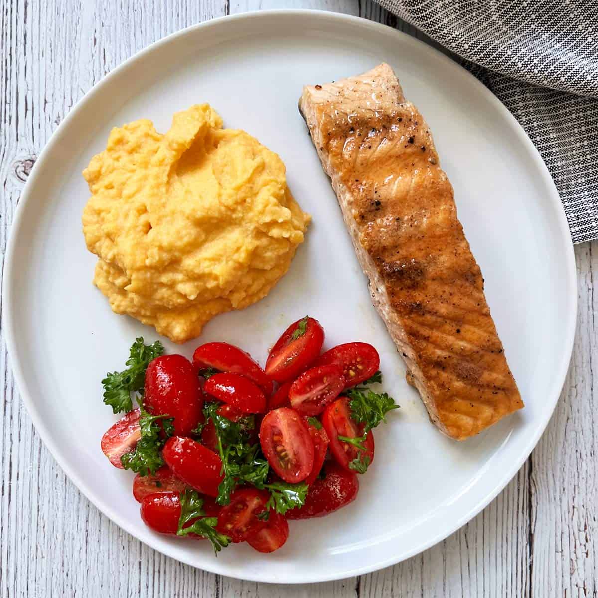 Mashed butternut squash is served with salmon and a tomato salad.