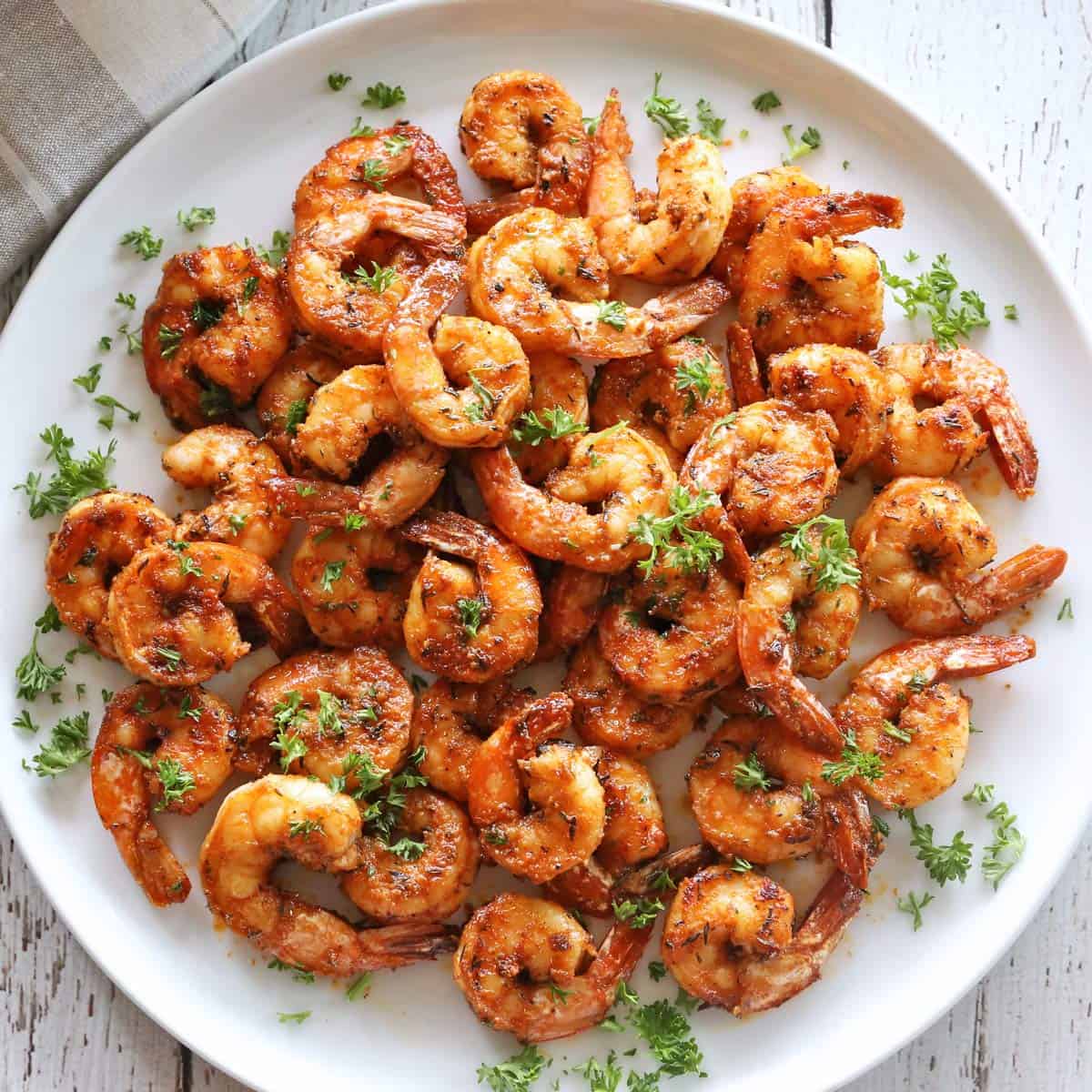 Sautéed shrimp are served on a white plate, garnished with chopped parsley.