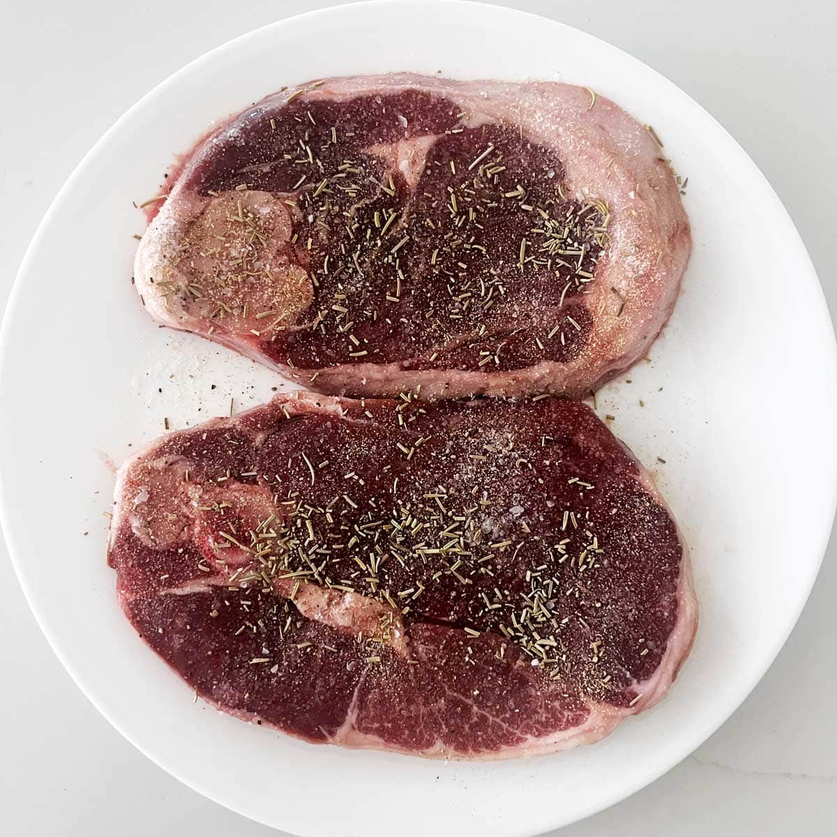 Lamb steaks are seasoned with salt, pepper, and dried rosemary.