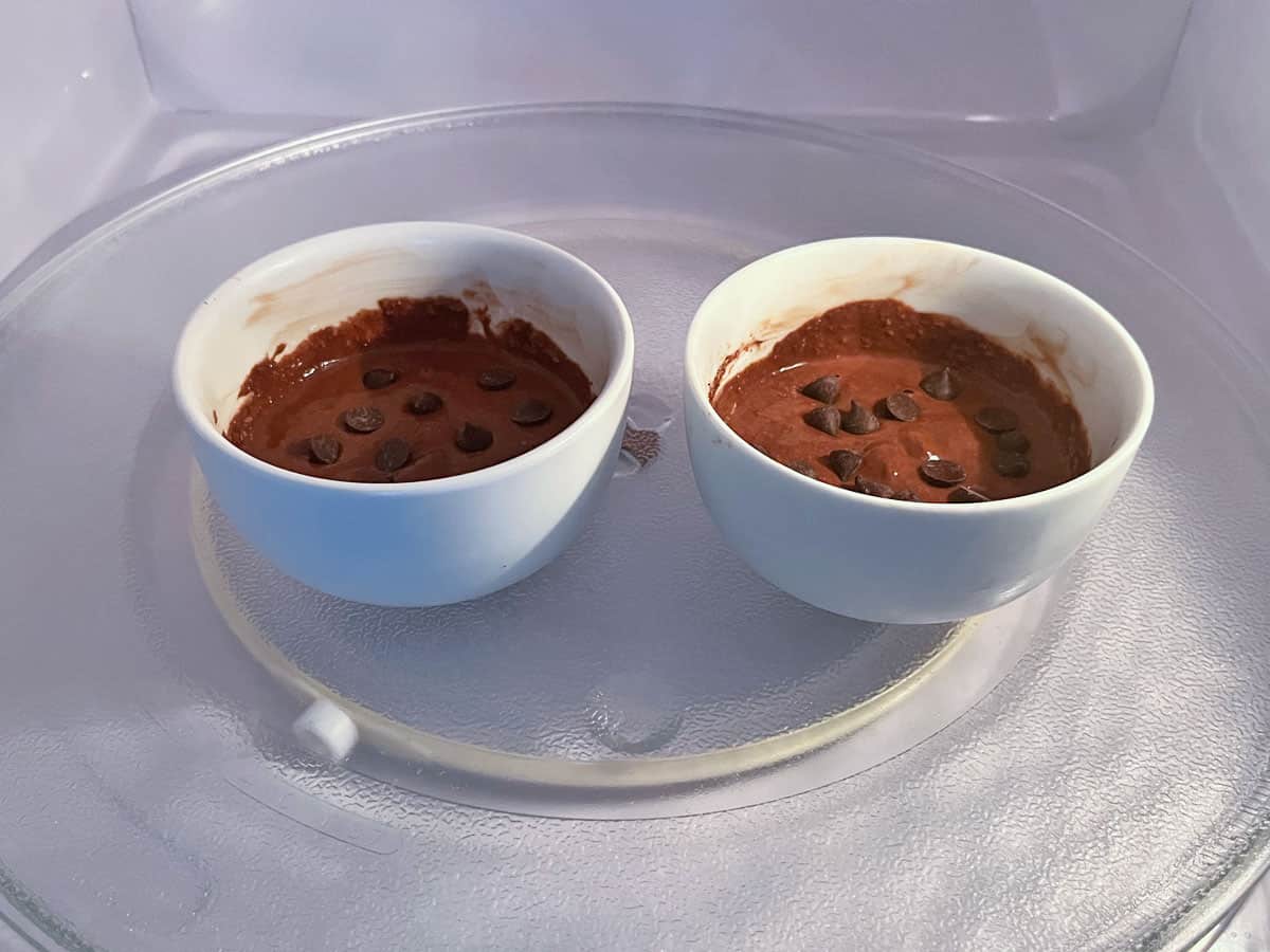Two bowls of chocolate mug cake in the microwave.