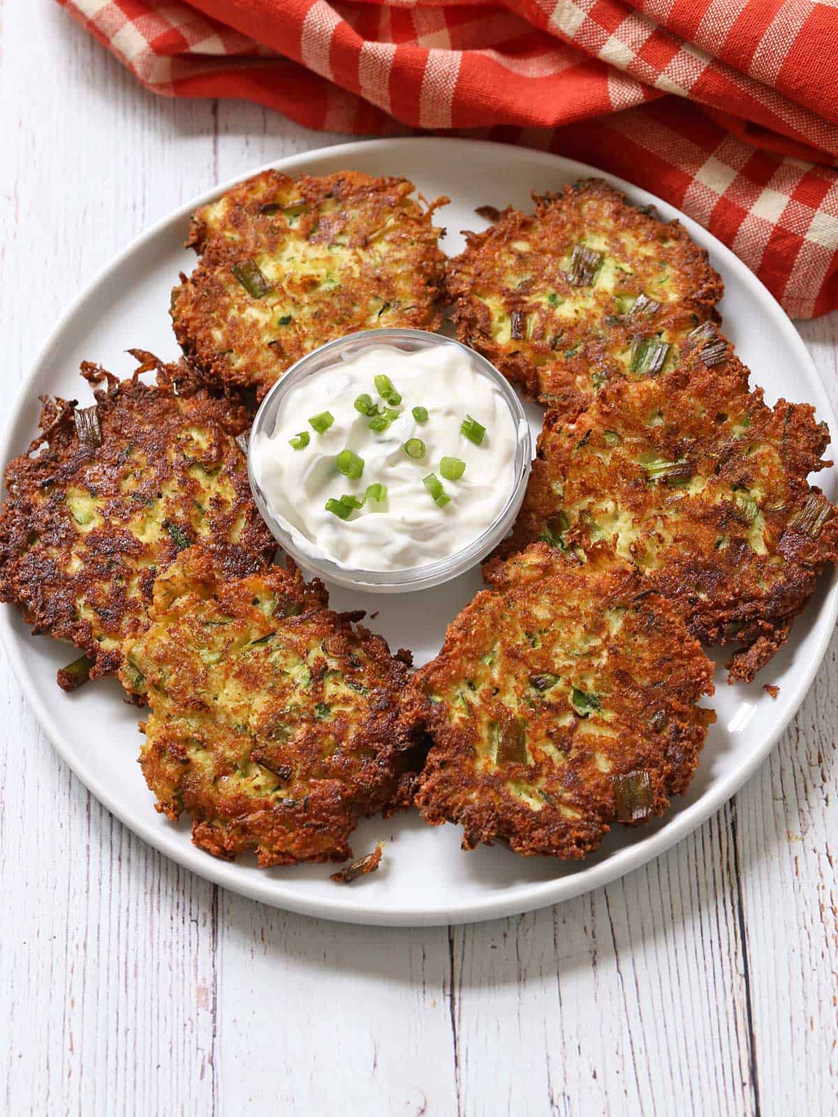 Zucchini fritters are served on a plate with a dip.