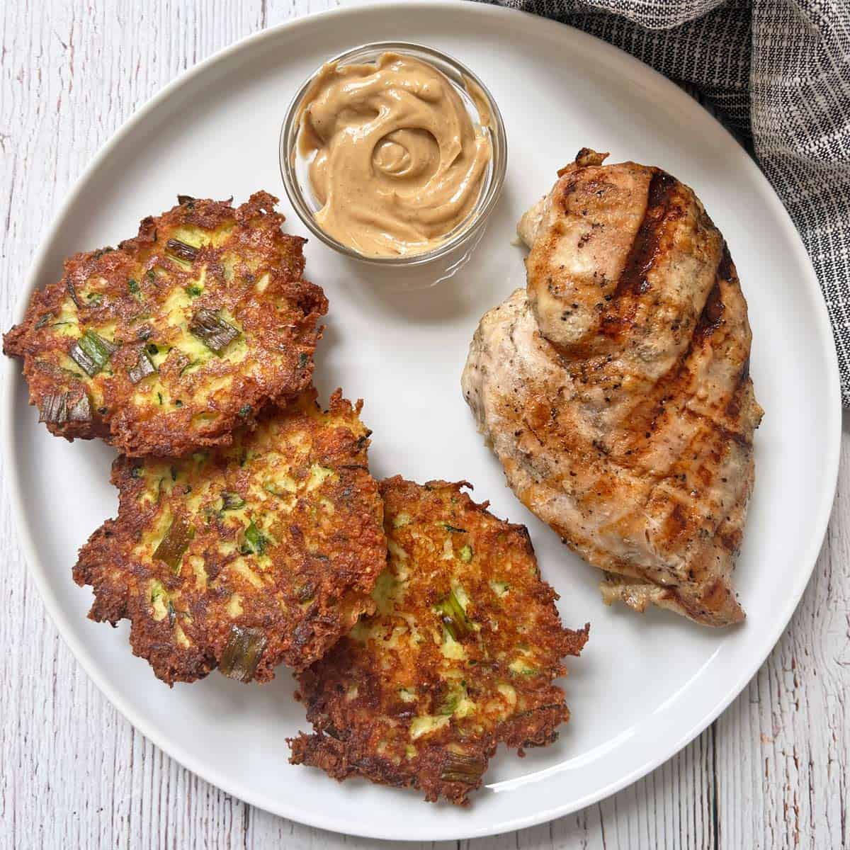 Zucchini fritters are served with grilled chicken breast and sriracha mayo.