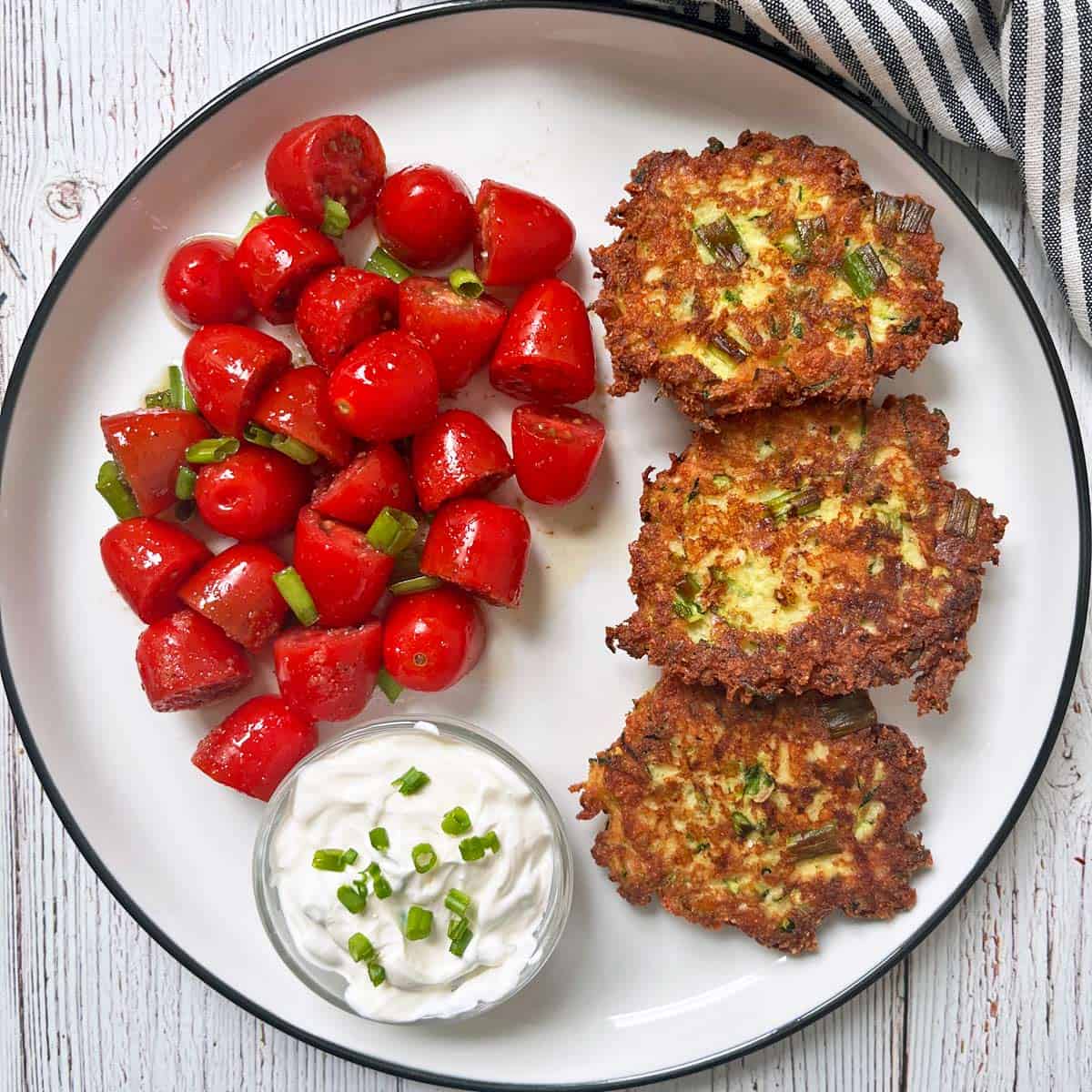 Zucchini fritters are served with a sour cream dip and tomato salad.