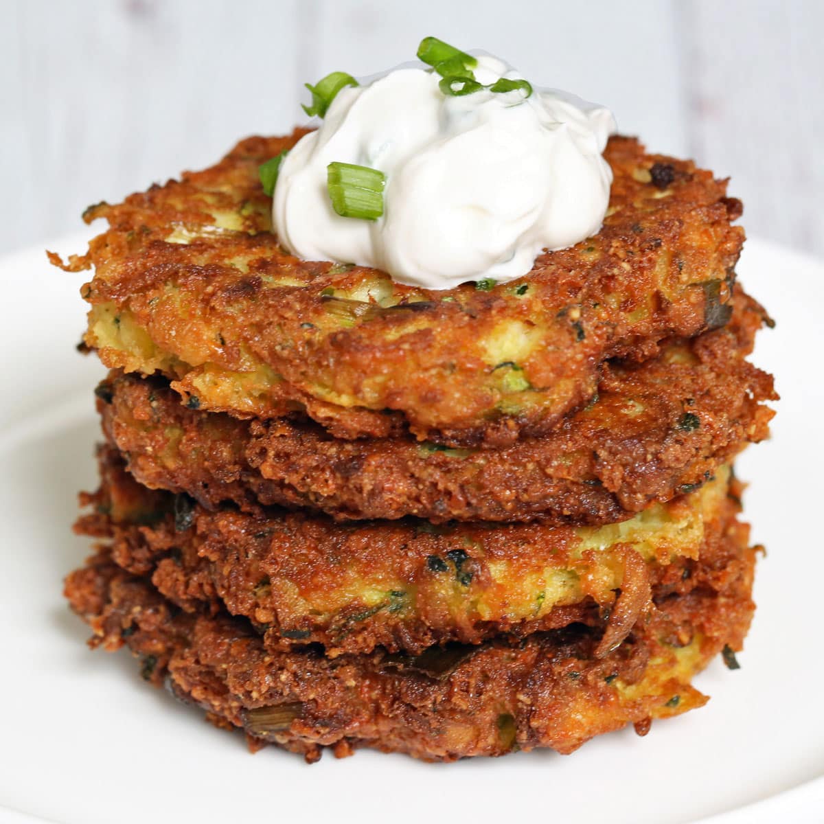 Zucchini fritters are stacked on a plate and topped with sour cream dip.