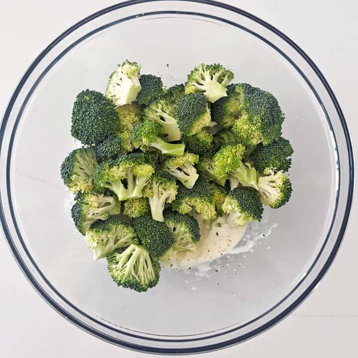 Adding the broccoli florets to the dressing in the bowl.