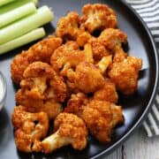 Buffalo cauliflower is served on a black plate with celery and blue cheese dip.
