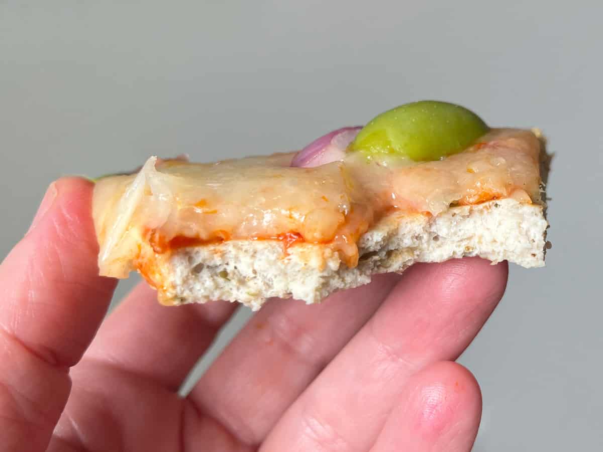A hand holds a half-eaten chicken pizza crust to show its texture.
