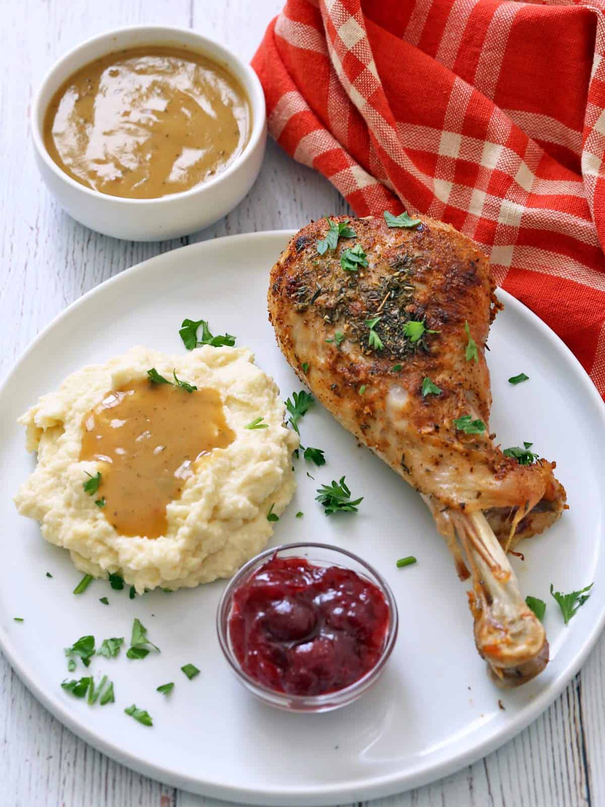 A thanksgiving plate with turkey drumstick, mashed cauliflower, gravy, and cranberry sauce.