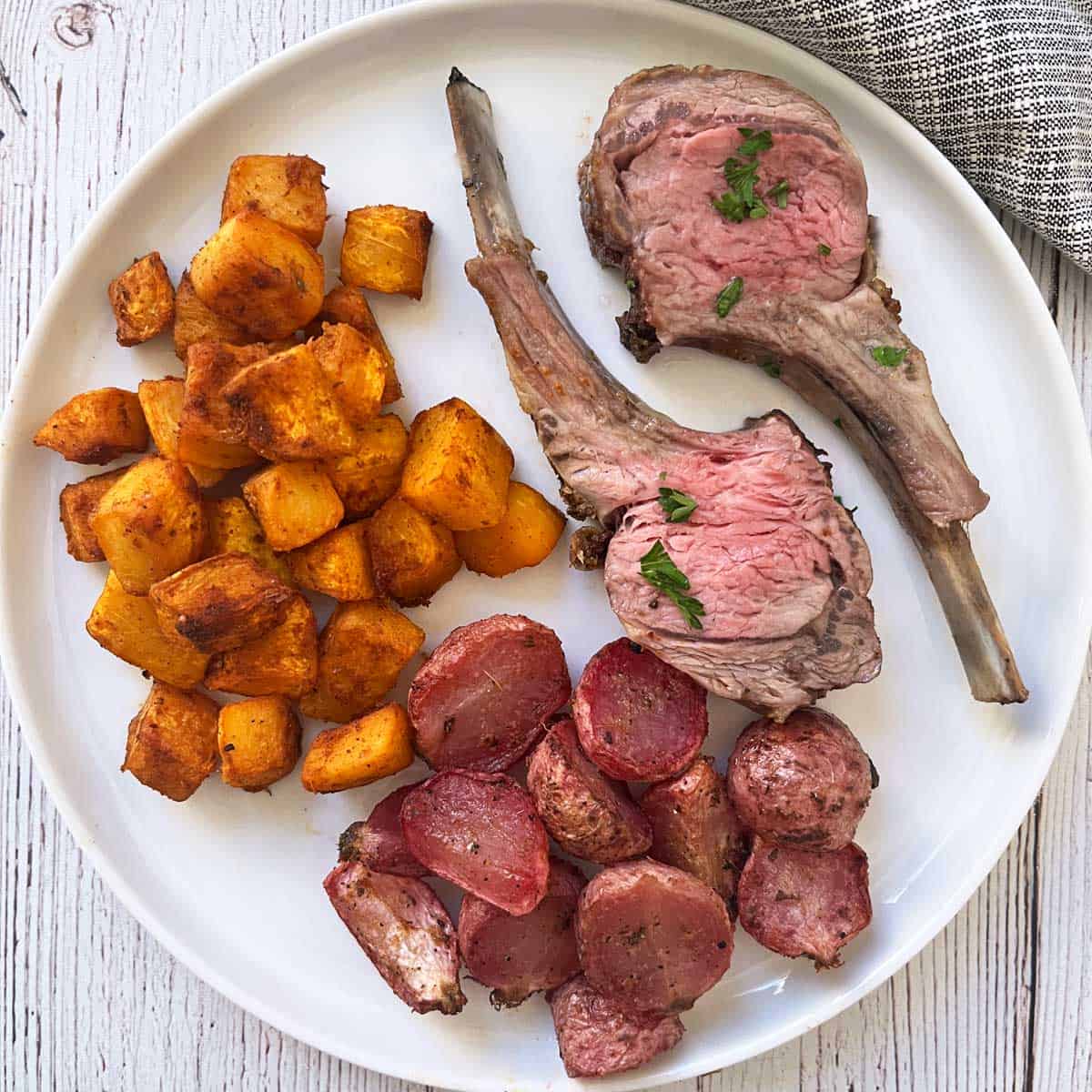 Two lamb ribs from a rack of lamb are served with roasted pumpkin and radishes.