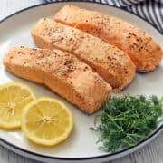 Poached salmon is served on a white plate with lemon and dill.