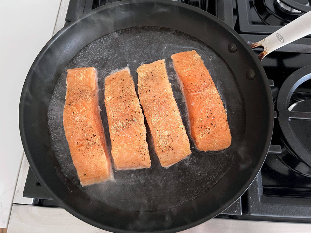Four salmon fillets are poached in a large skillet.