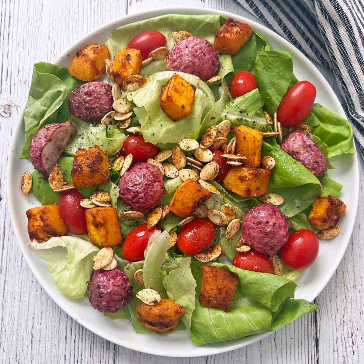 A salad with lettuce, tomatoes, roasted radishes, roasted pumpkin, and pumpkin seeds.
