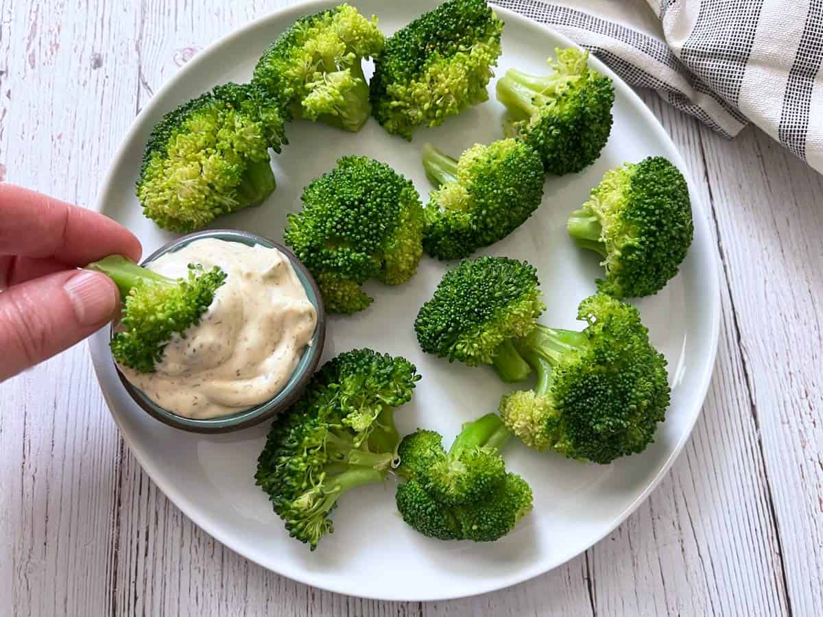Steamed broccoli is dipped into tartar sauce.