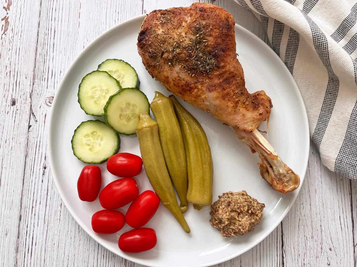 A leftover turkey leg is served cold with veggies, pickles, and mustard.